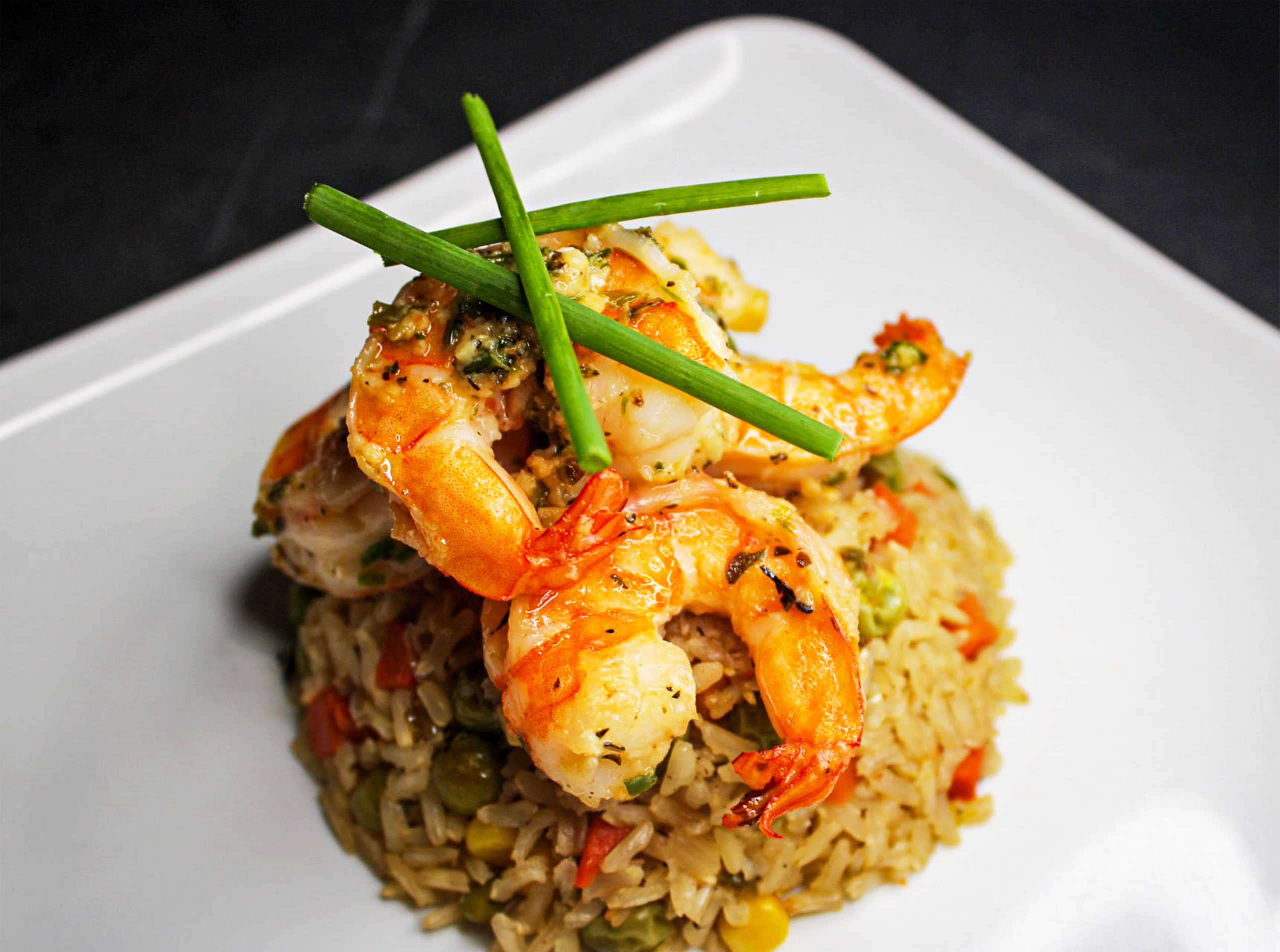 Delicious fried rice topped with prawns, garnished with scallions, beautifully plated.
