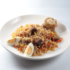 A savory dish of jollof rice served with meat, vegetables, and boiled eggs on a white plate.