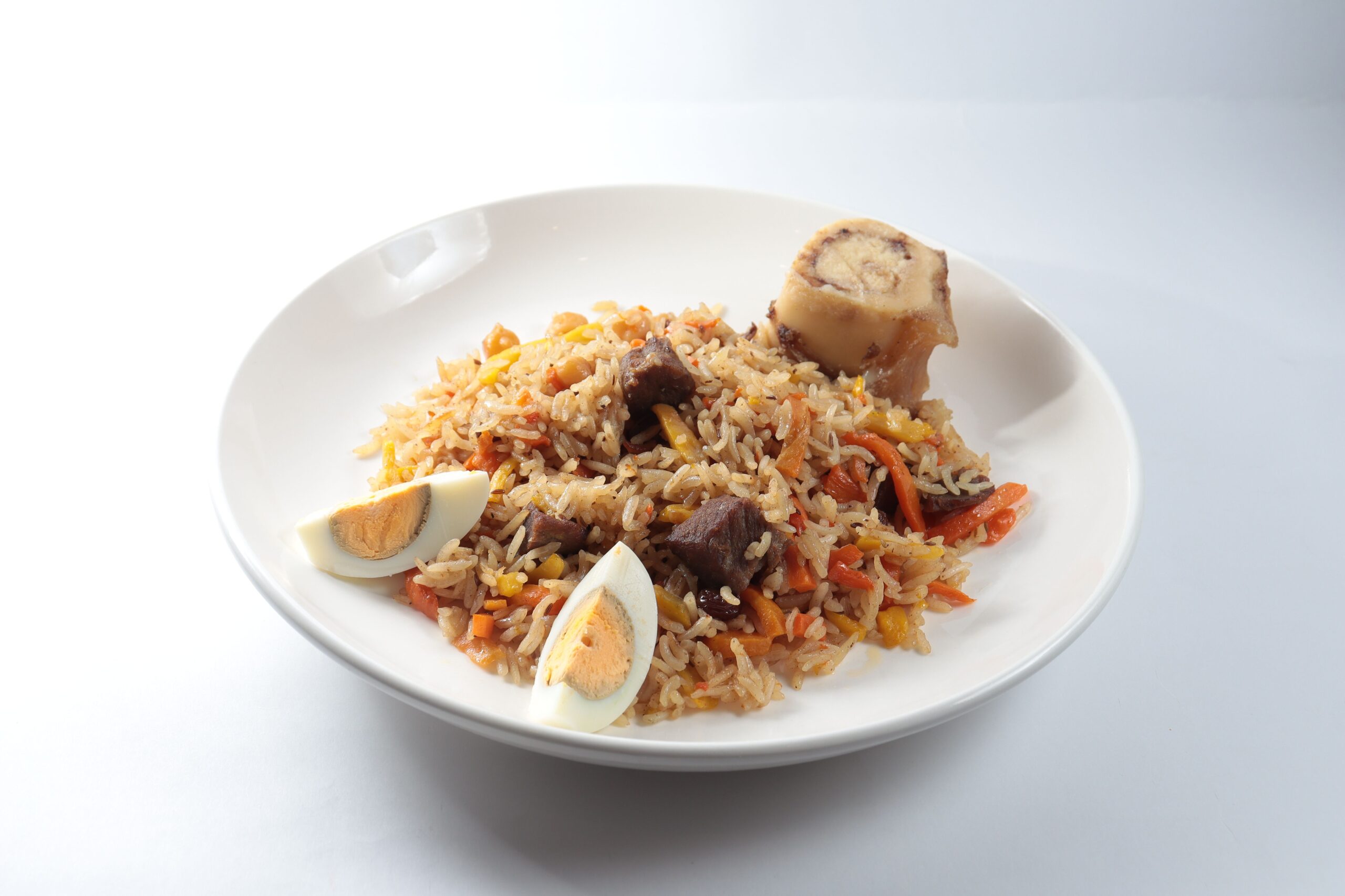 A savory dish of jollof rice served with meat, vegetables, and boiled eggs on a white plate.